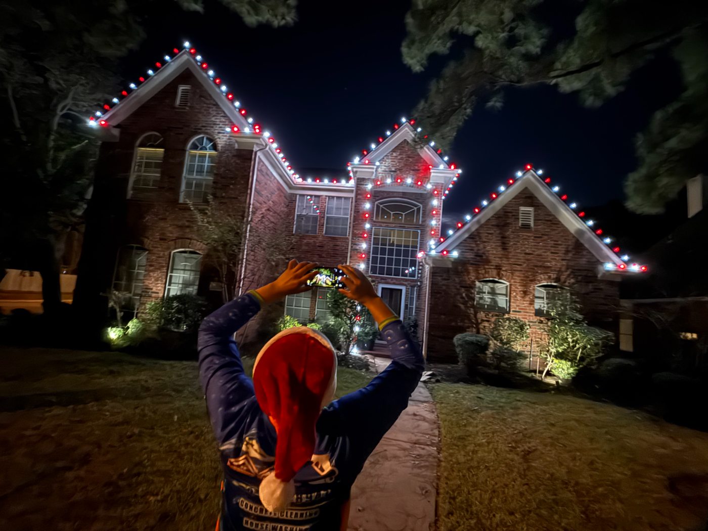 A child in a Santa hat photographing a house lit in red and white